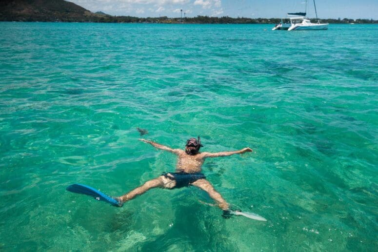 A guy in fins and a mask swims in lagoon during a catamaran tour on the island of Mauritius