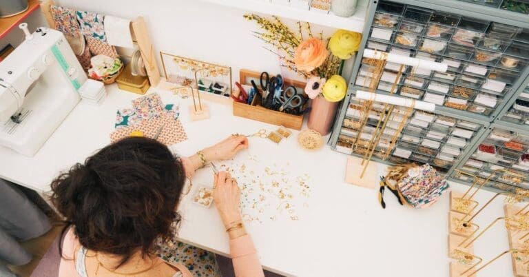 An overhead view of a brunette woman sitting at a desk while she works on making a bracelet.