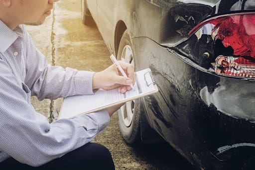 Driver documenting rear-end collision damage while assessing liability after a car accident