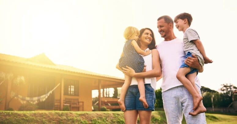 A man and a woman are walking together outdoors, and each pf them is holding a different child.